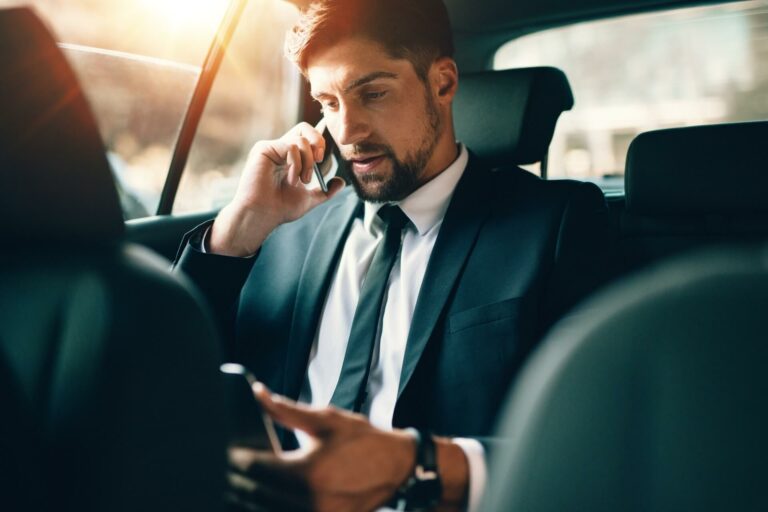 a man inside a car speaking on the phone and working on his laptop